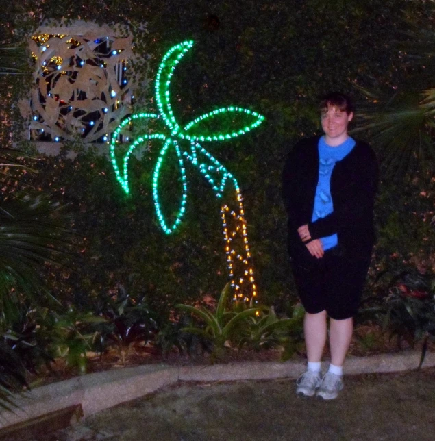 a woman poses in front of a palm tree covered in christmas lights