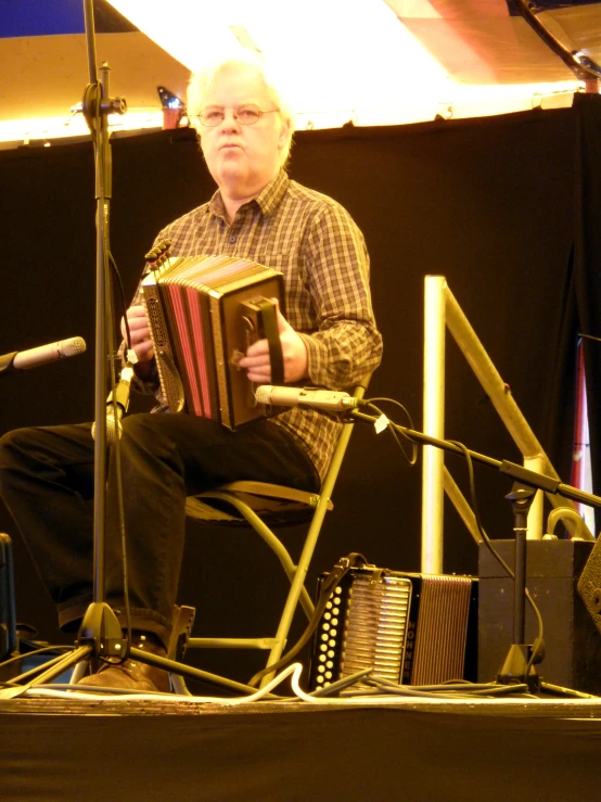 an elderly man playing an accordion while standing on stage