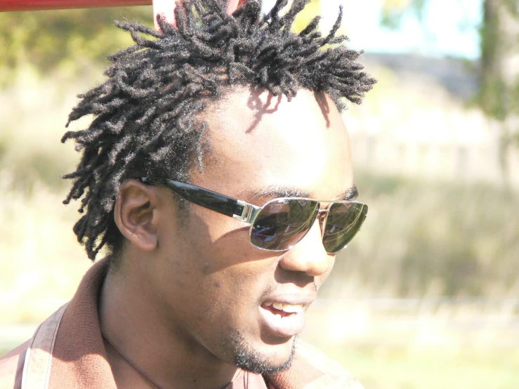 a man with dreadlocks wearing shades standing by a fence