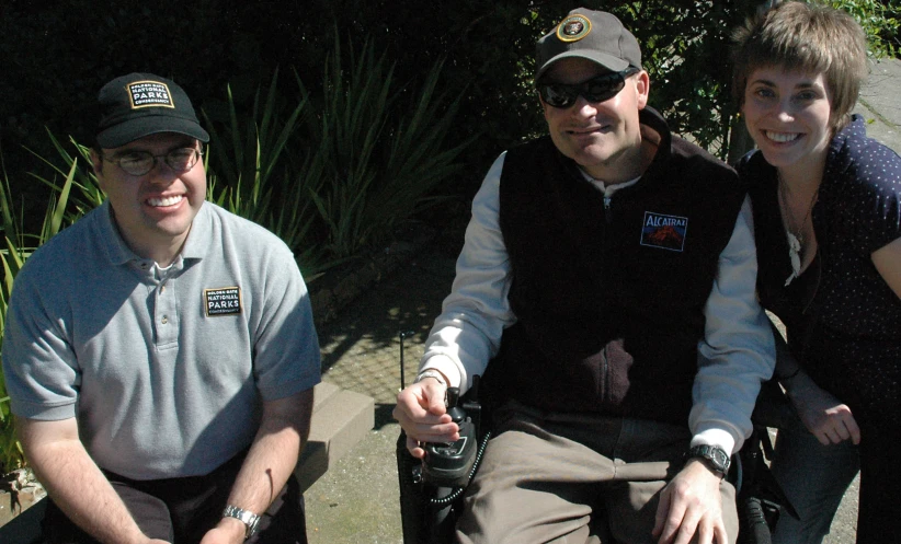 a man sits in a wheel chair with two other people