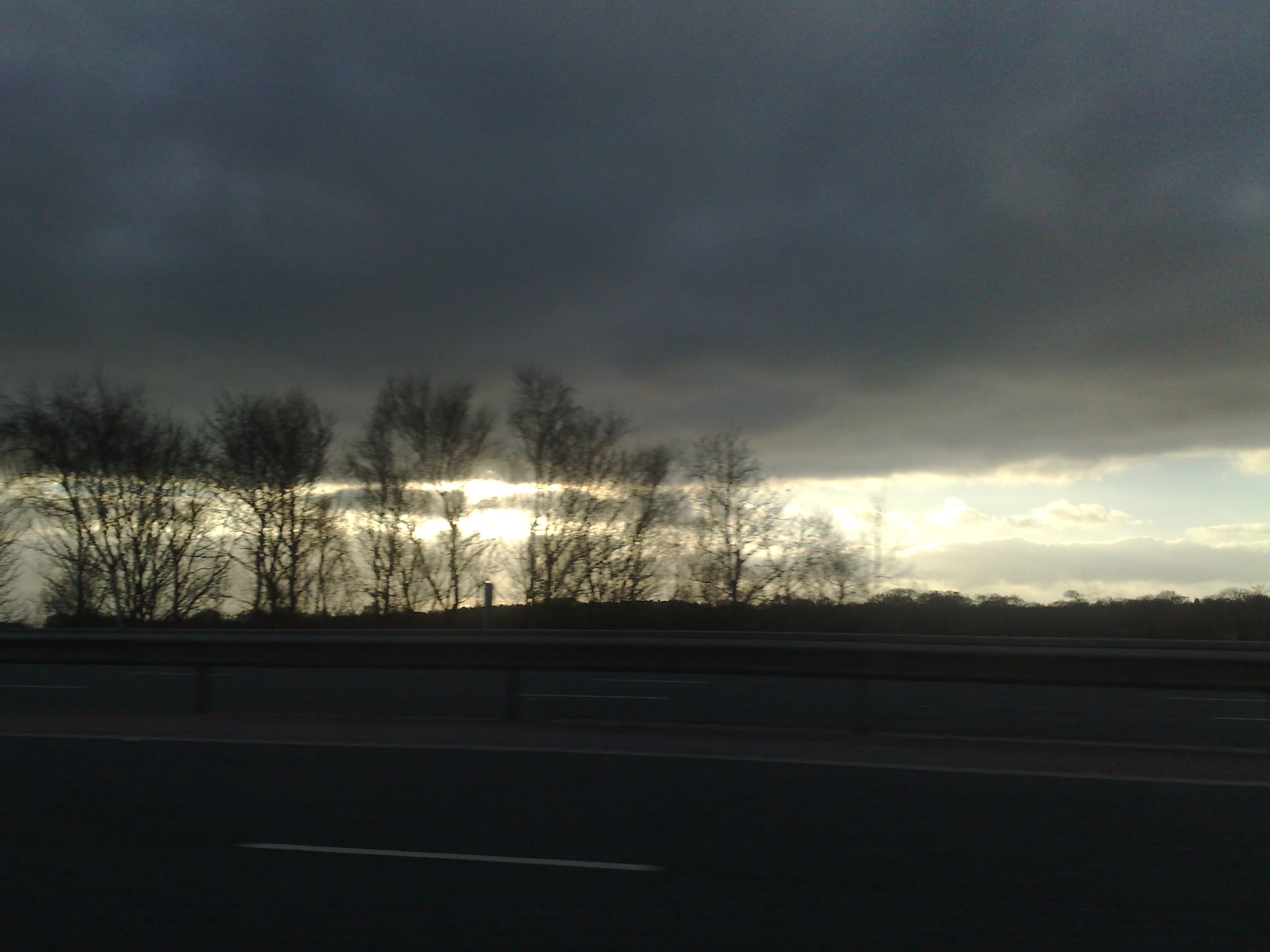 a road near trees with the sun coming out of behind it