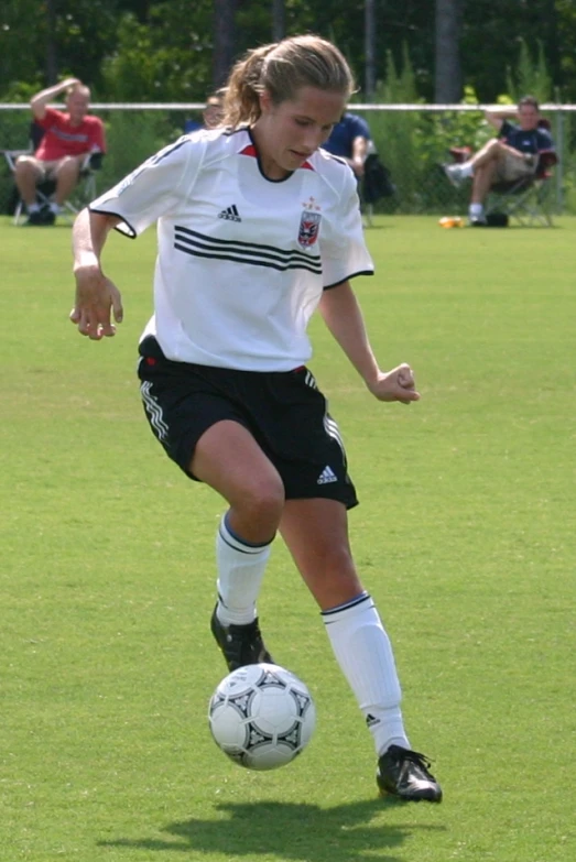 woman kicking soccer ball with people watching in background