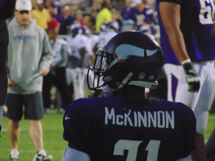 a close up of a football player wearing a helmet with other players and coaches in the background