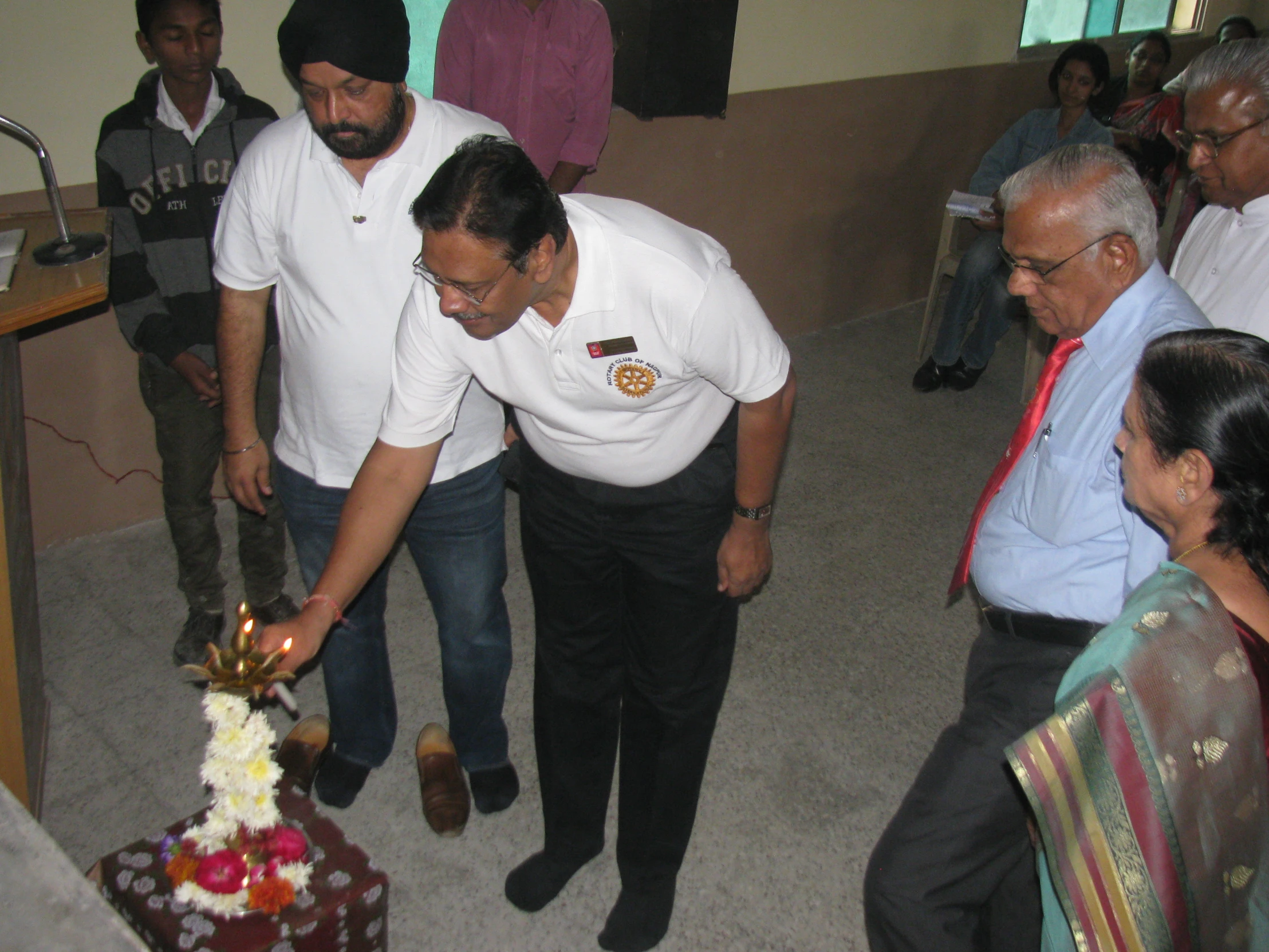 a group of people are gathered around a man  a cake