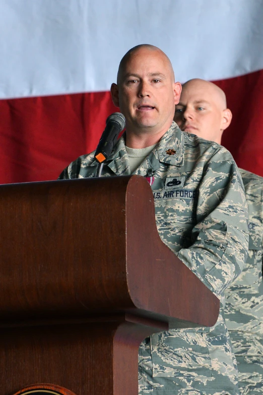 two men wearing uniform standing at a podium with an american flag behind them