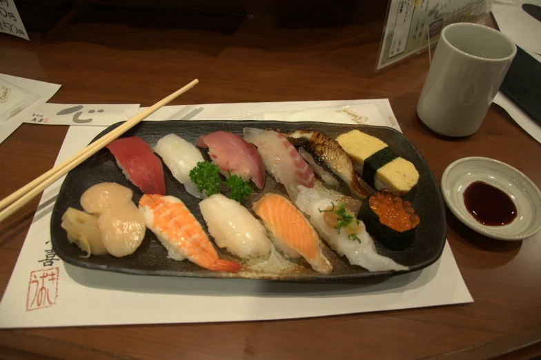 a plate with many kinds of sushi, chopsticks, and a drink