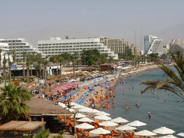 a crowded beach with white umbrellas and buildings around it