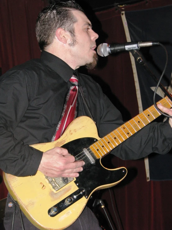 a man is asleep next to a microphone and a yellow electric guitar