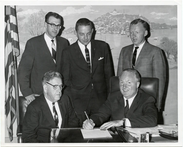 men in suits and ties around a desk signing papers
