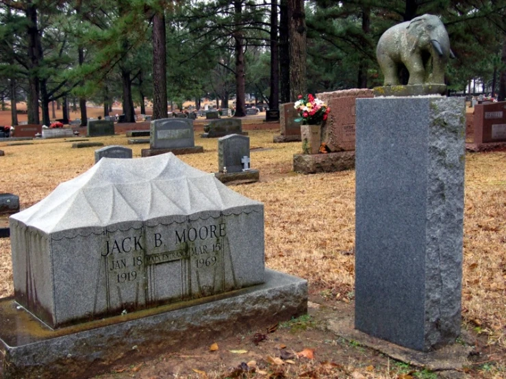 two tombstones stand in a wooded cemetery with an elephant statue