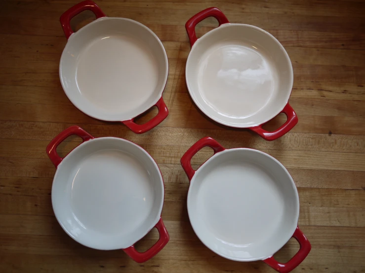 four white dishes with red handles lay atop a wood table