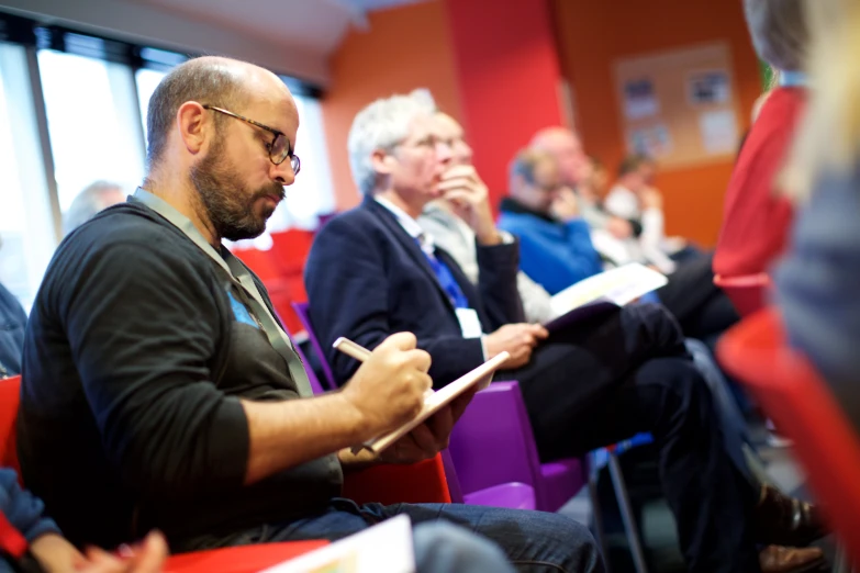 there are many people sitting in chairs and writing