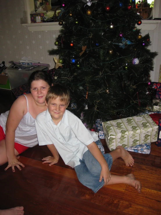 two children sitting on the floor next to a christmas tree