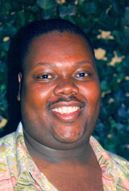 a black man in floral shirt smiling for the camera