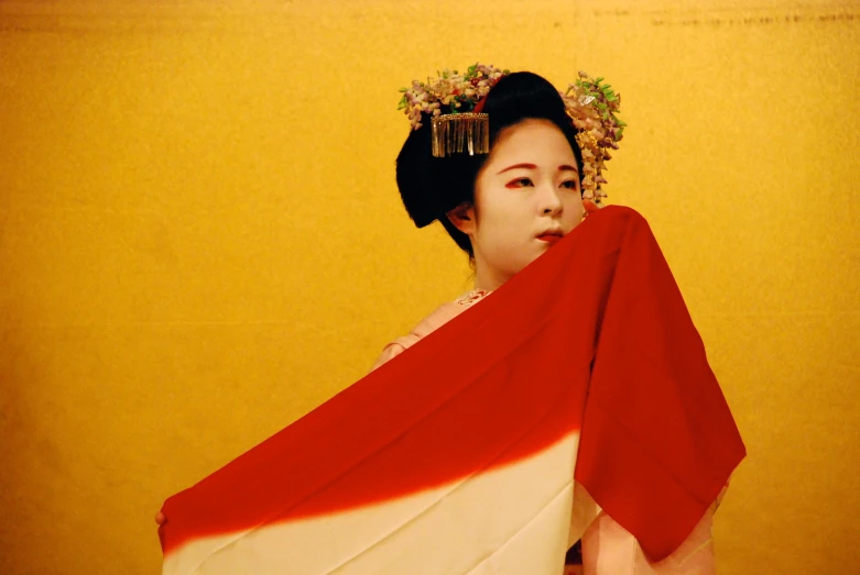 a geisha wearing red and white sits with an orange and pink material