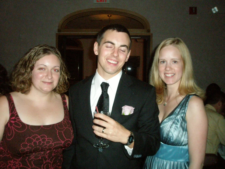 two ladies in dresses and a man in a suit pose for a po