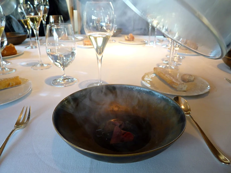 a bowl on a dining table with silverware and wine glasses