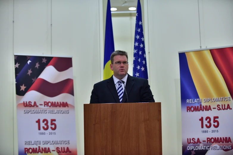 a man standing behind a wooden podium with an american flag banner