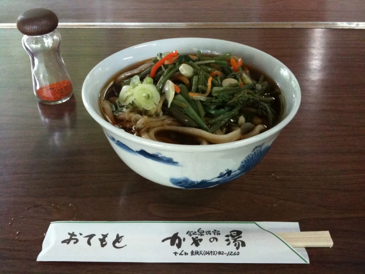 a bowl of noodles and vegetables served with an oriental note board