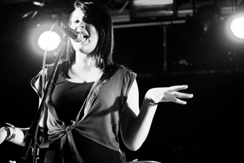 woman singing into microphone at night with lights in background