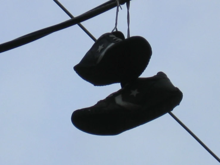 pair of tennis shoes hanging from wire with clear sky in background