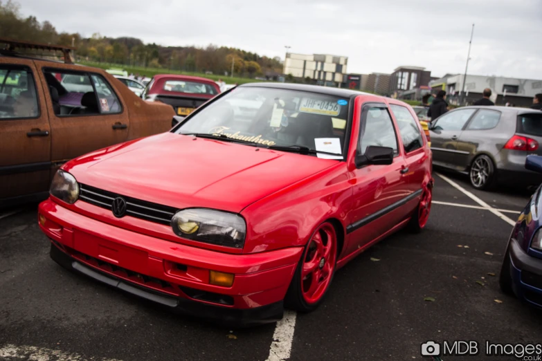 a red golf car is parked in a lot next to other cars