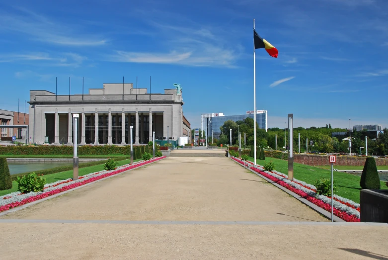 a flagpole stands above a long road with red flowered borders