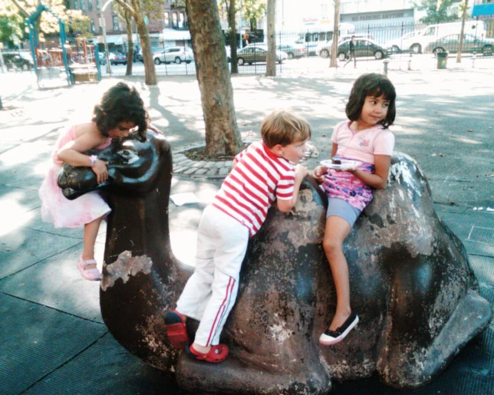 two girls and a boy sitting on a cement camel