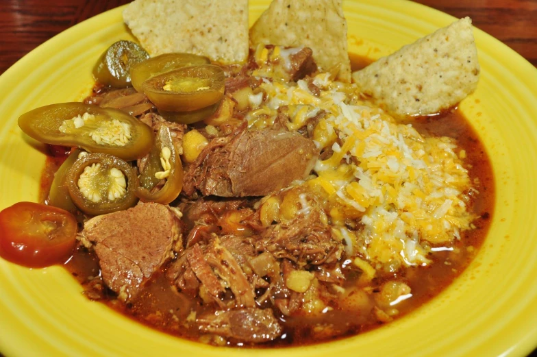 a yellow plate containing an enchilada soup with chili, peppers, tortillas, and bread