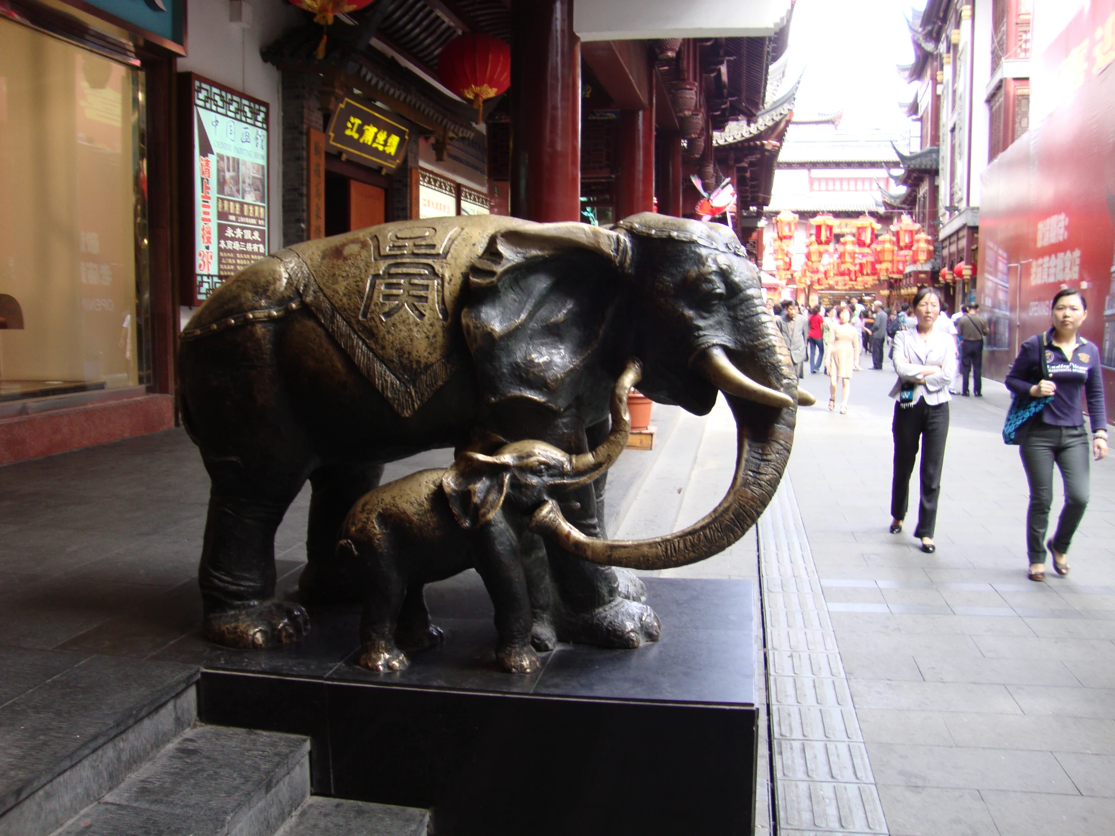 two adult elephants and a baby elephant on a sidewalk