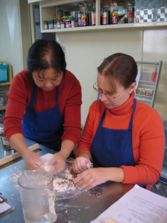 two women in red and blue aprons making dough