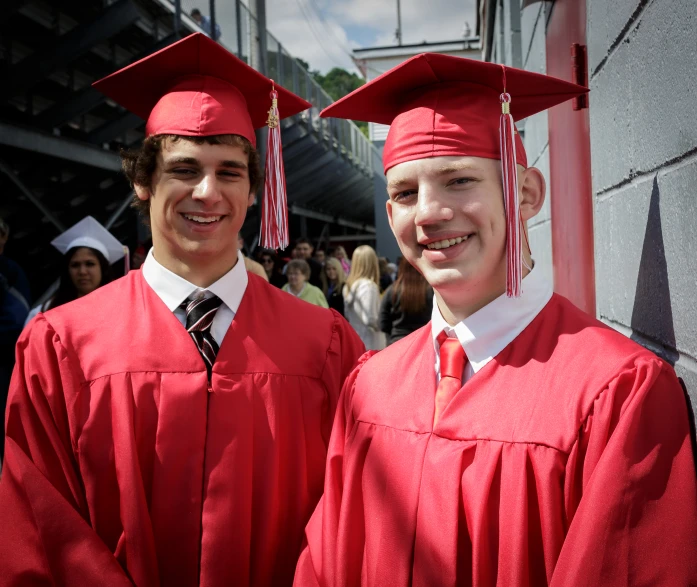 two young men standing side by side in red caps and gowns