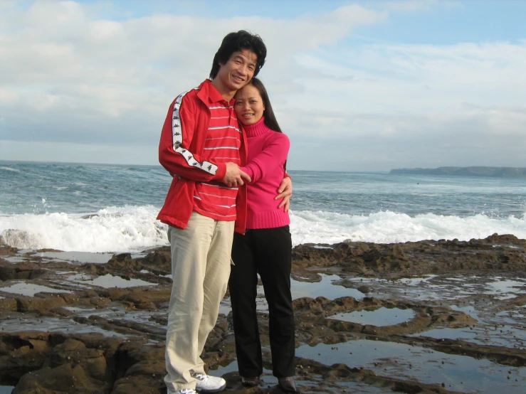 an asian couple hugging on a rocky shoreline