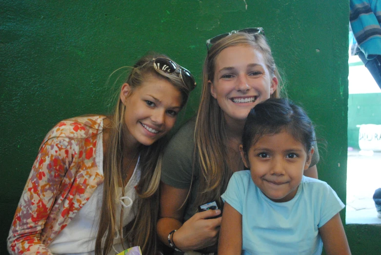 three girls smile with one of them holding a cell phone