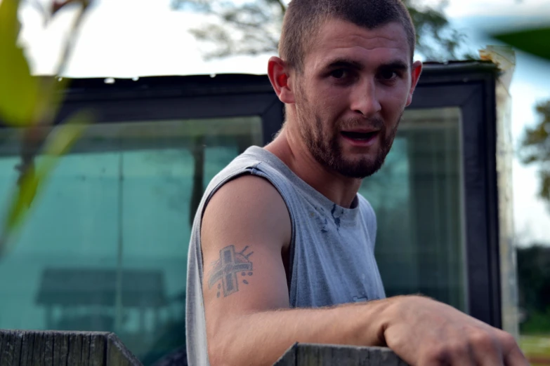 a man with tattoos on his arm is behind a fence