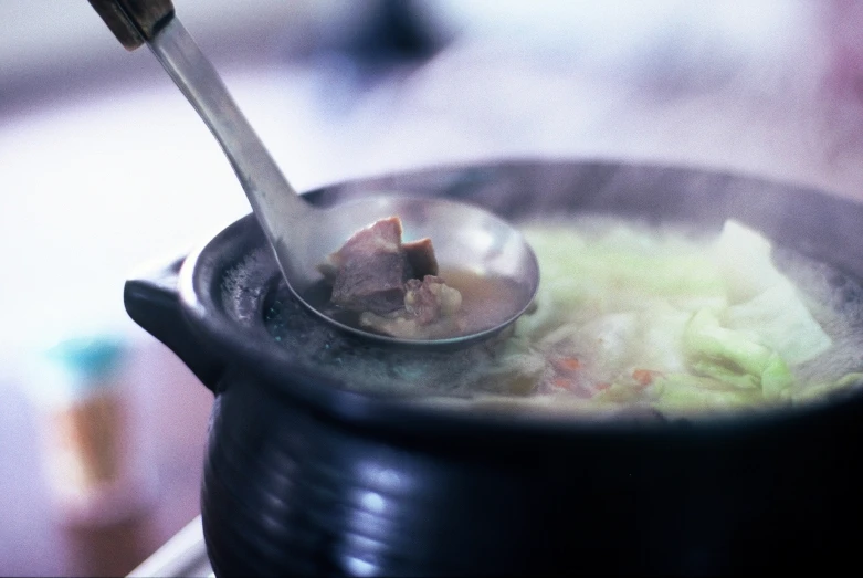 a spoon filled with soup and meat on top of it