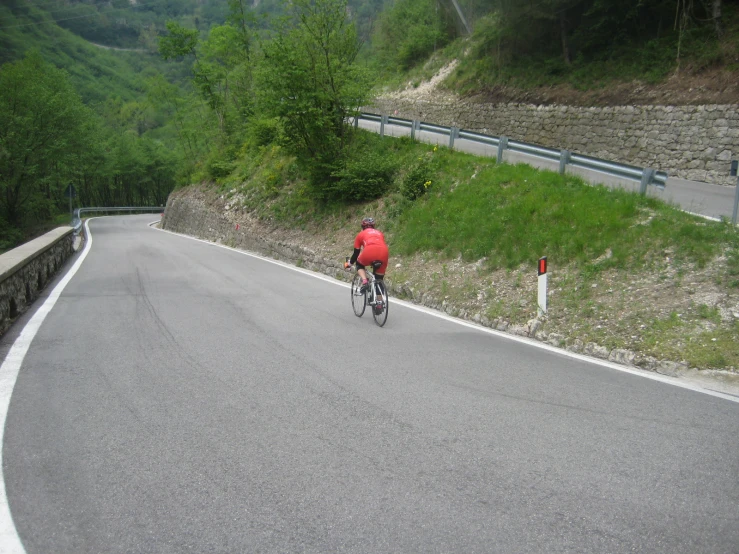 the bicyclist in red is riding down the winding road