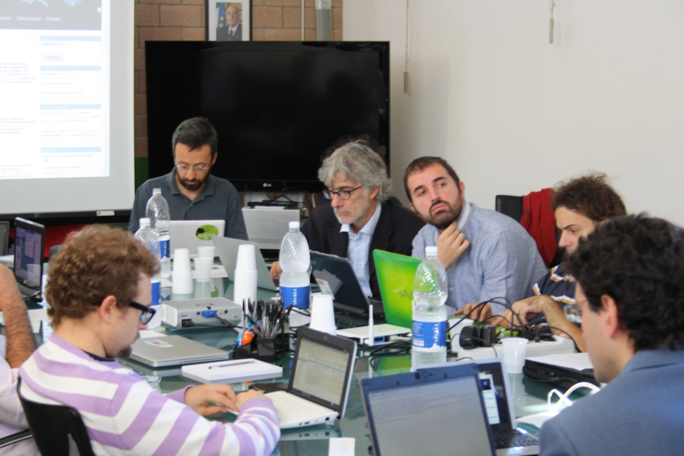 a group of people sitting at a table and some with laptops