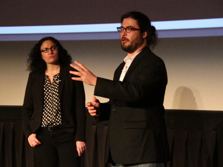 two men and a woman on a stage speaking