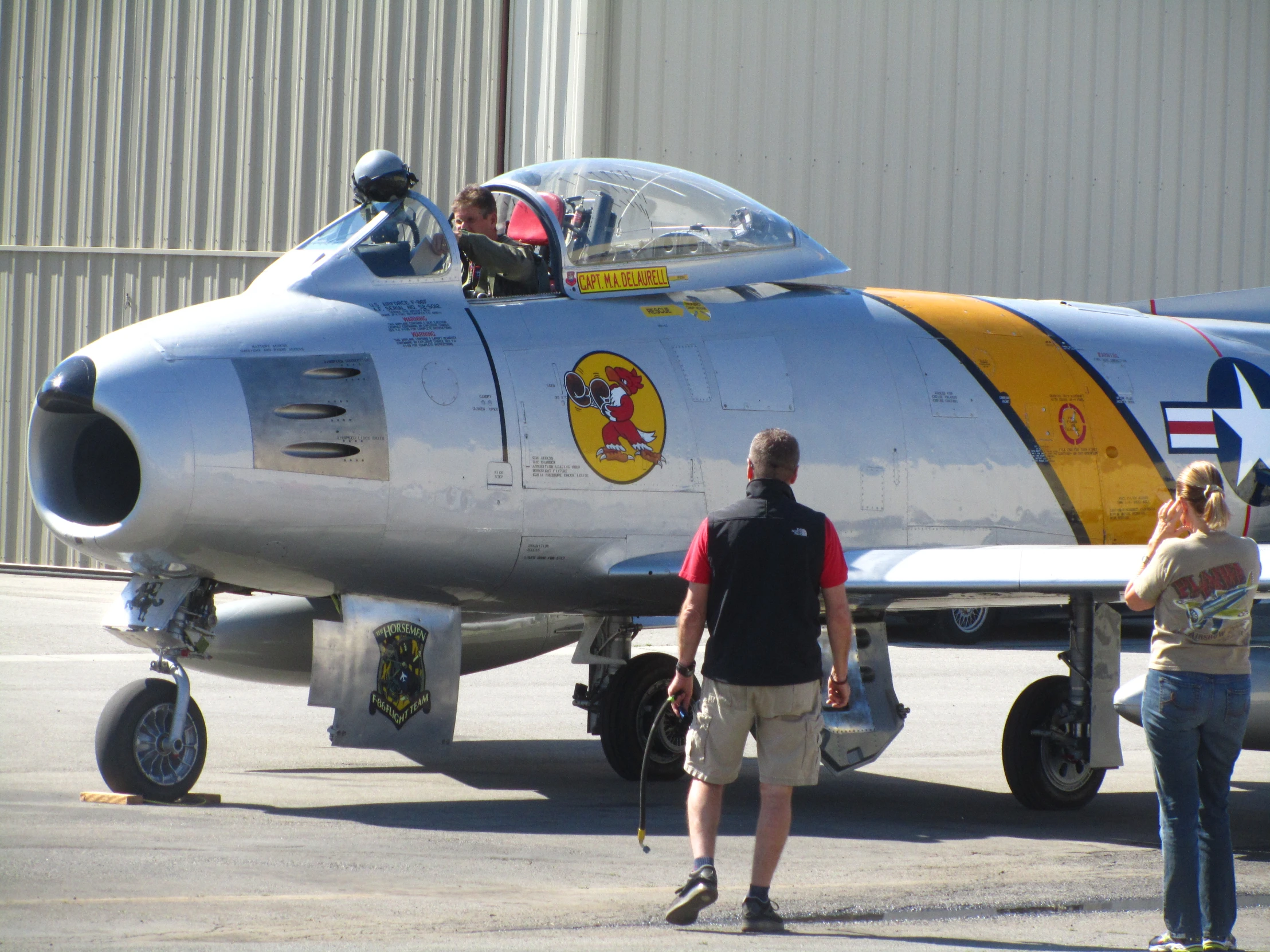 a silver jet with a yellow stripe and a woman standing in front
