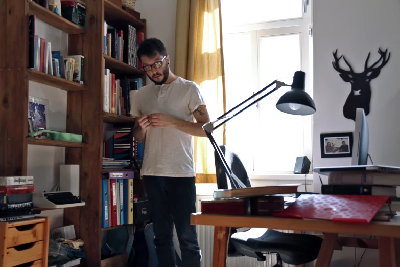 a man with glasses is standing in a room with a desk