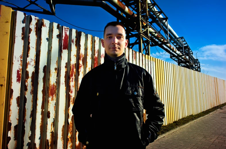a man in black stands next to a rusted building