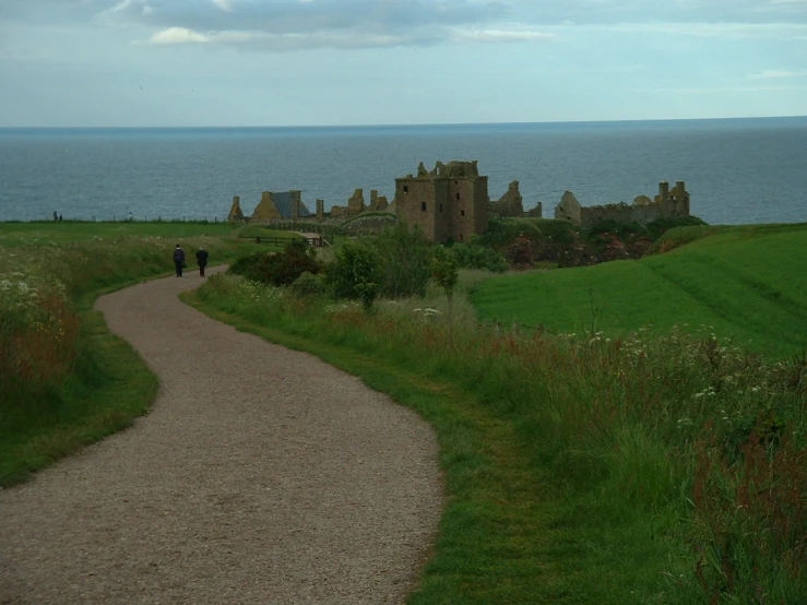 two people walking down a path next to a castle