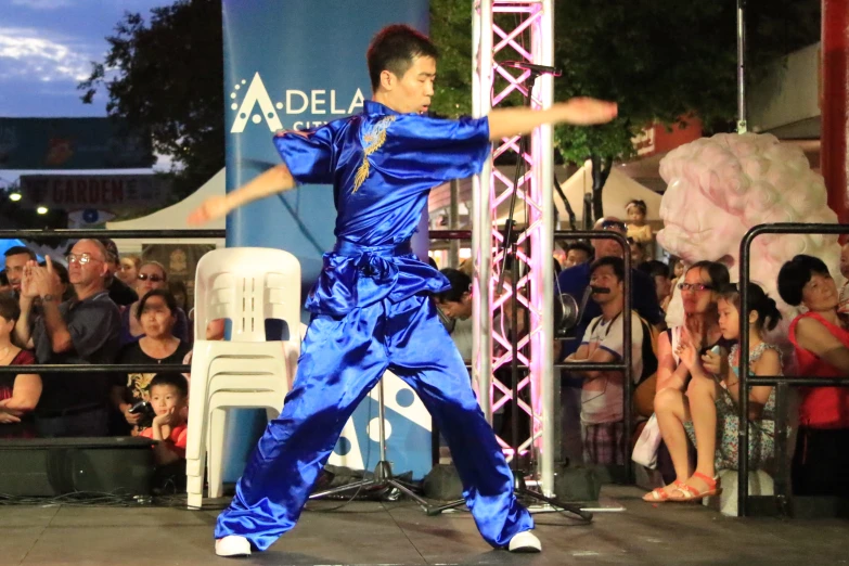 man in blue jumpsuit standing on stage near a crowd