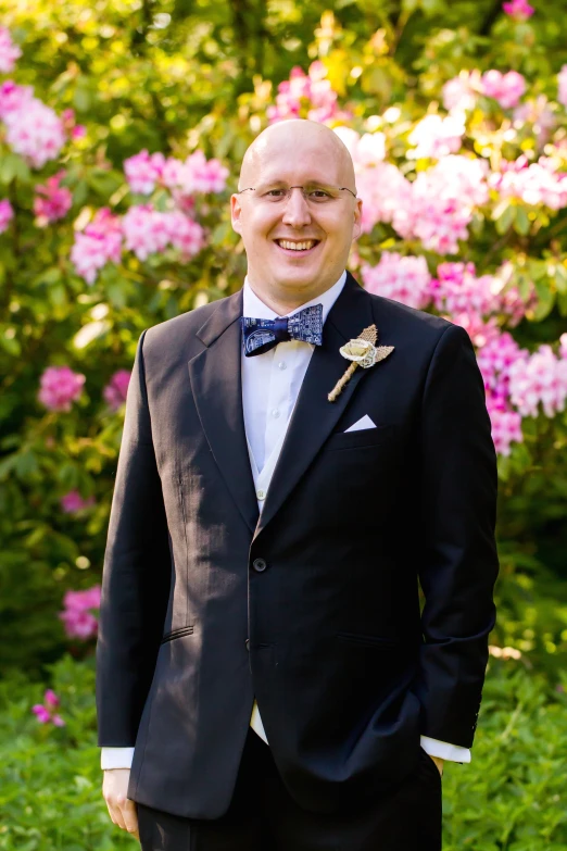 a man in a tuxedo standing near some flowers