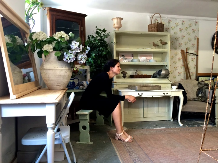 a woman sitting on a bench in a room with many furniture and potted plants