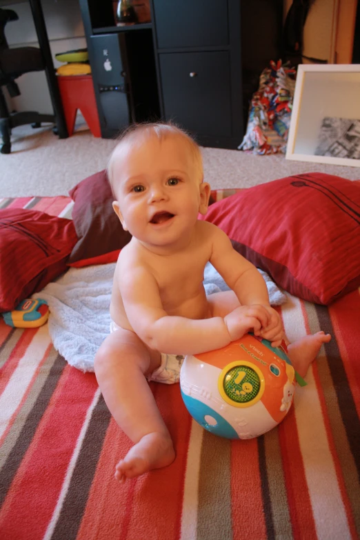 a baby sitting on top of a bed near pillows