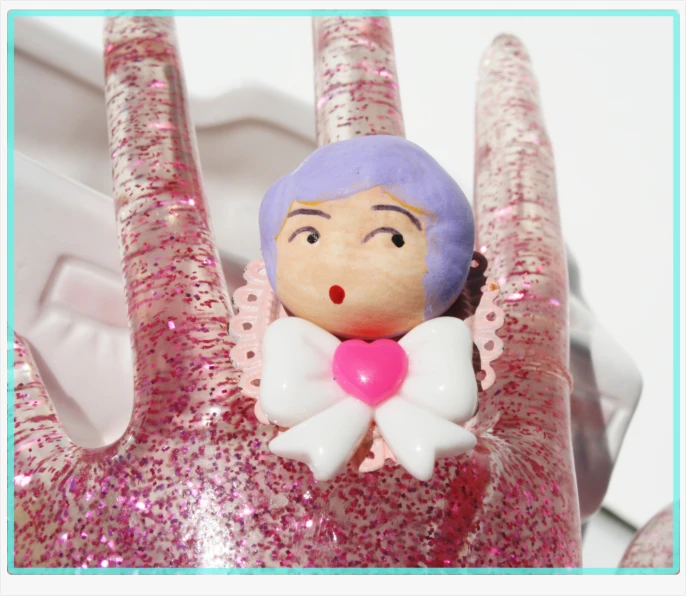 a toy doll on a fingers holding onto a pink heart