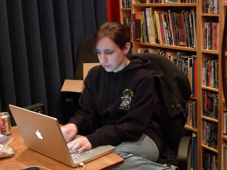 a girl sits at her laptop while reading a book in front of the camera