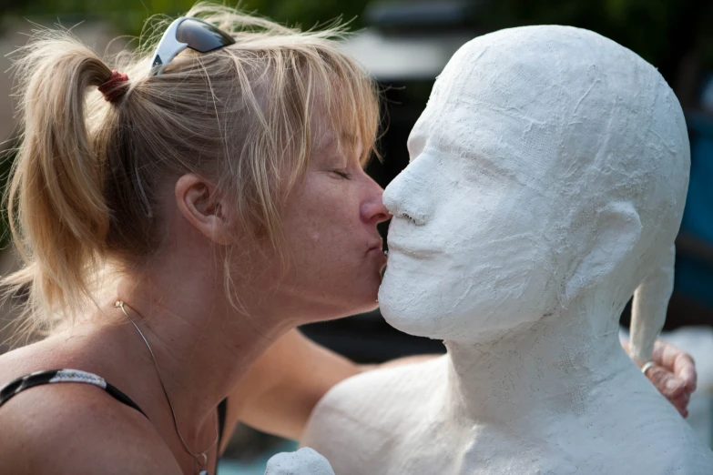 a woman licking the head of a white sculpture